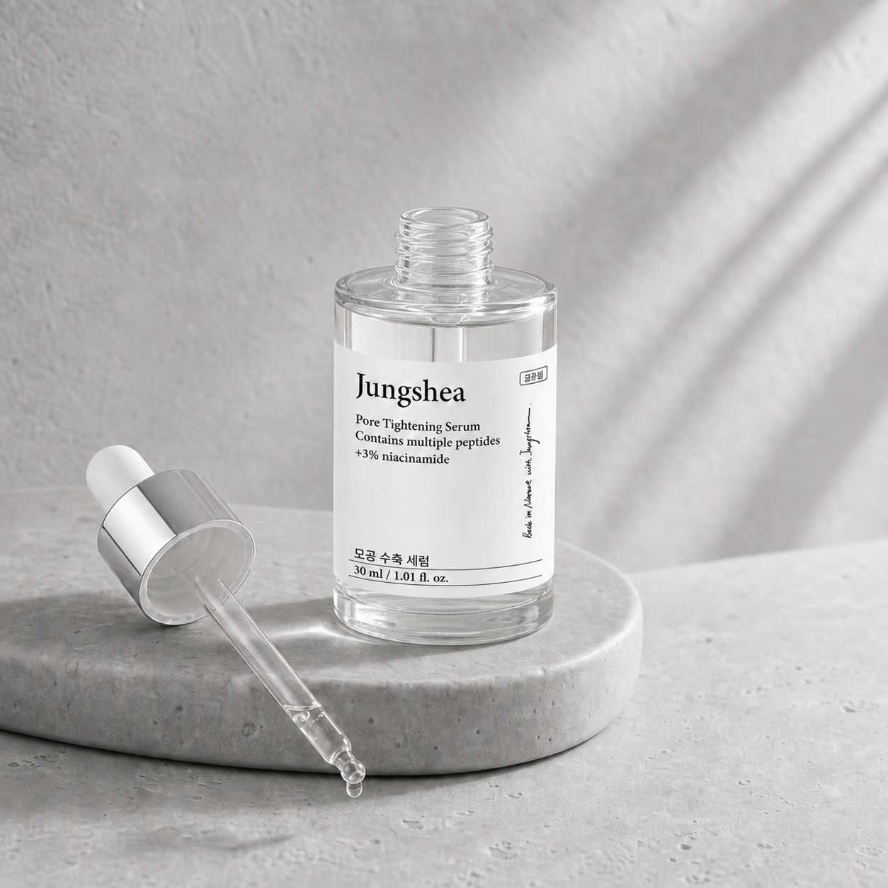 Open Jungshea serum bottle and glass dropper on a gray stone pedestal