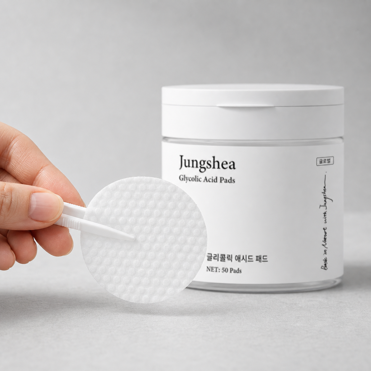 Hand holding a textured exfoliating pad with tweezers in front of the Jungshea jar
